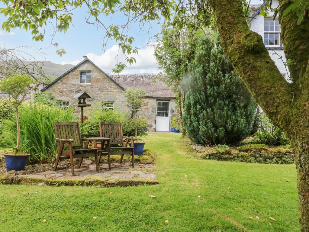 a garden with two chairs and a table in front of a house at Inglis Nook Cottage in Lochearnhead