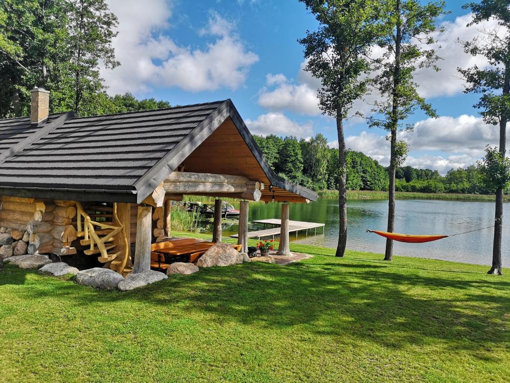 a log cabin with a hammock next to a lake at Pirties namelis ant ežero kranto in Trakai