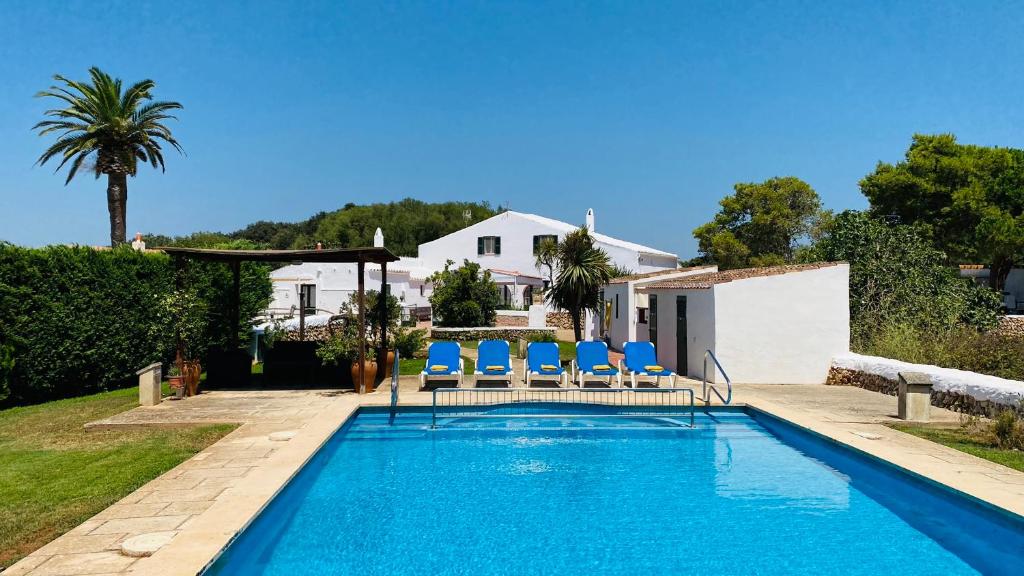 a swimming pool with blue chairs and a house at Finca TONI in Alaior