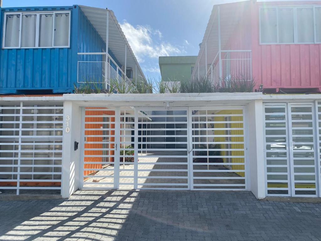 a white gate in front of some colorful buildings at Loft container central c/ estacionamento in Pelotas