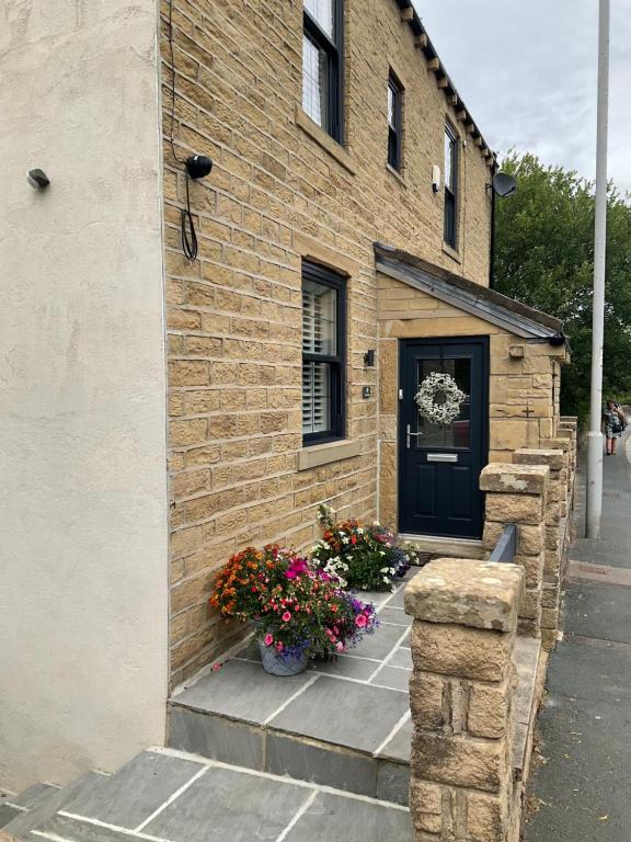 een bakstenen gebouw met een zwarte deur en bloemen bij The Gables in Haworth