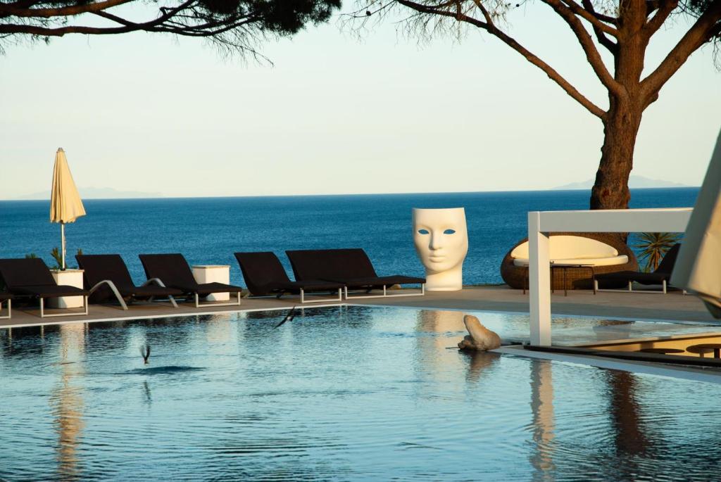 einen Pool mit Stühlen und das Meer im Hintergrund in der Unterkunft Resort Capo Bianco in Porto Azzurro