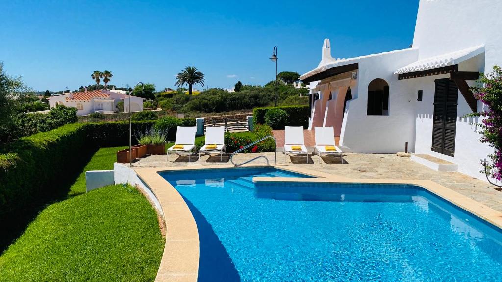 a swimming pool in front of a house with chairs and a house at Villa Bini Kim in Binibeca