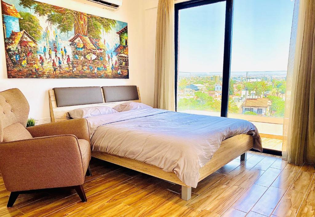 a bedroom with a bed and a chair and a large window at BALI SUITES 505 in Larnaka