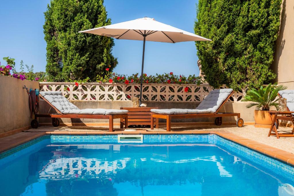 a swimming pool with two chairs and an umbrella at Villa Sion in Cala Mendia