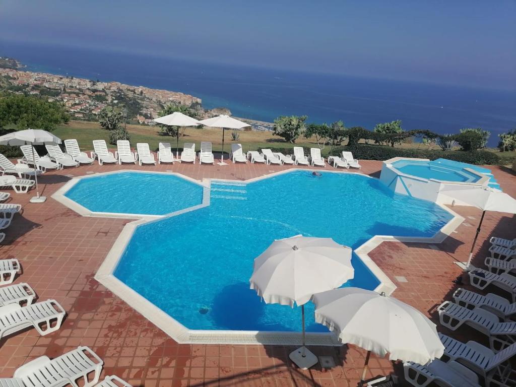a swimming pool with umbrellas and chairs and the ocean at Bilocale RESIDENCE MARASUSA in Parghelia