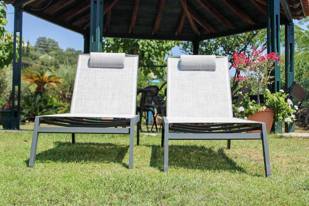 two white chairs sitting in the grass under a gazebo at Giovanni Group Apartments in Syvota