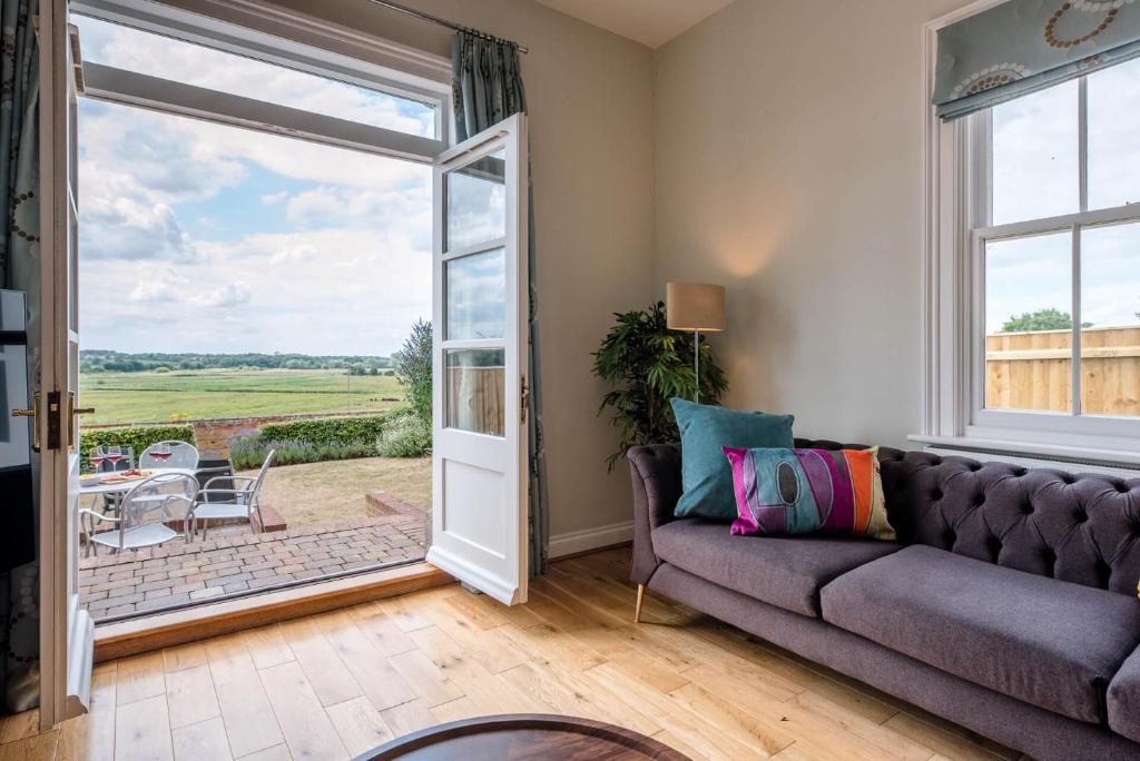 een woonkamer met een bank en een glazen schuifdeur bij Sunset House Blythburgh Air Manage Suffolk in Halesworth