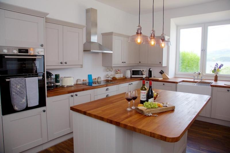 a kitchen with white cabinets and a wooden counter top at Creggans Cottage in Creggans