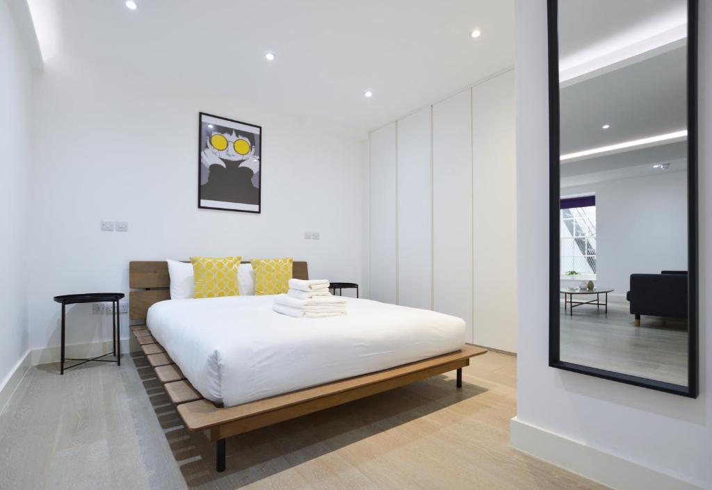 Un dormitorio con una cama blanca y un espejo. en Soho 22 Serviced Apartments by Concept Apartments, en Londres
