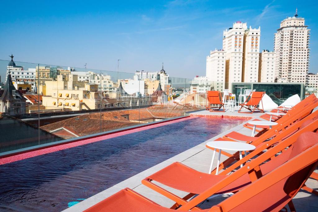 una piscina sul tetto di un edificio con sedie arancioni di Akeah Hotel Gran Vía a Madrid