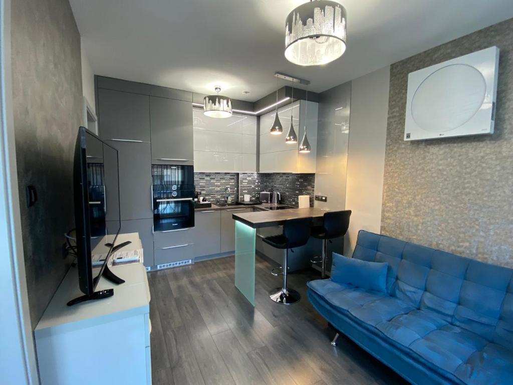 a living room with a blue couch and a kitchen at Noir Silvery Apartman in Szeged