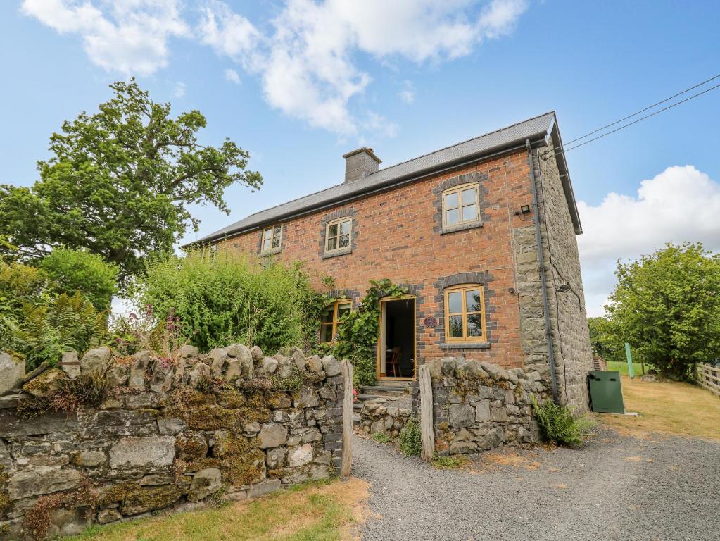 an old brick house with a stone wall at Byrdir Cottage in Llanwrthwl