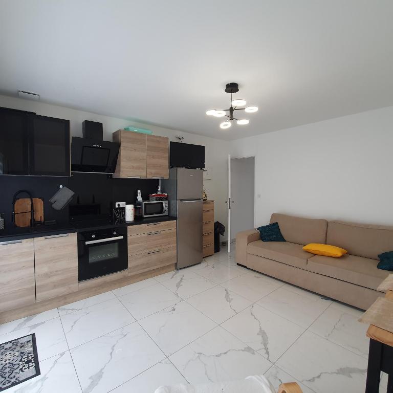 Una sala de estar con un sofá y una cocina. en Appartement EVR!CA - 1 place parking gratuit, en Le Perrier