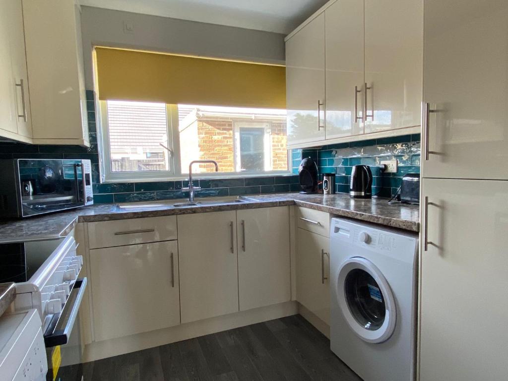 a kitchen with white cabinets and a washer and dryer at Four Seasons by the Sea in Peacehaven