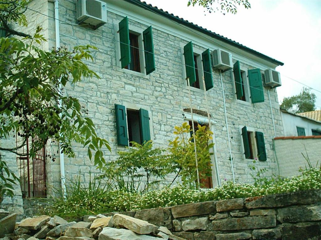 a stone building with green windows and a stone wall at Villa Ermis in Lákka