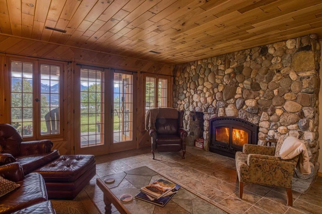 a living room with a stone wall with a fireplace at Pine Ridge, Log Home with Lake View and Backyard in Invermere