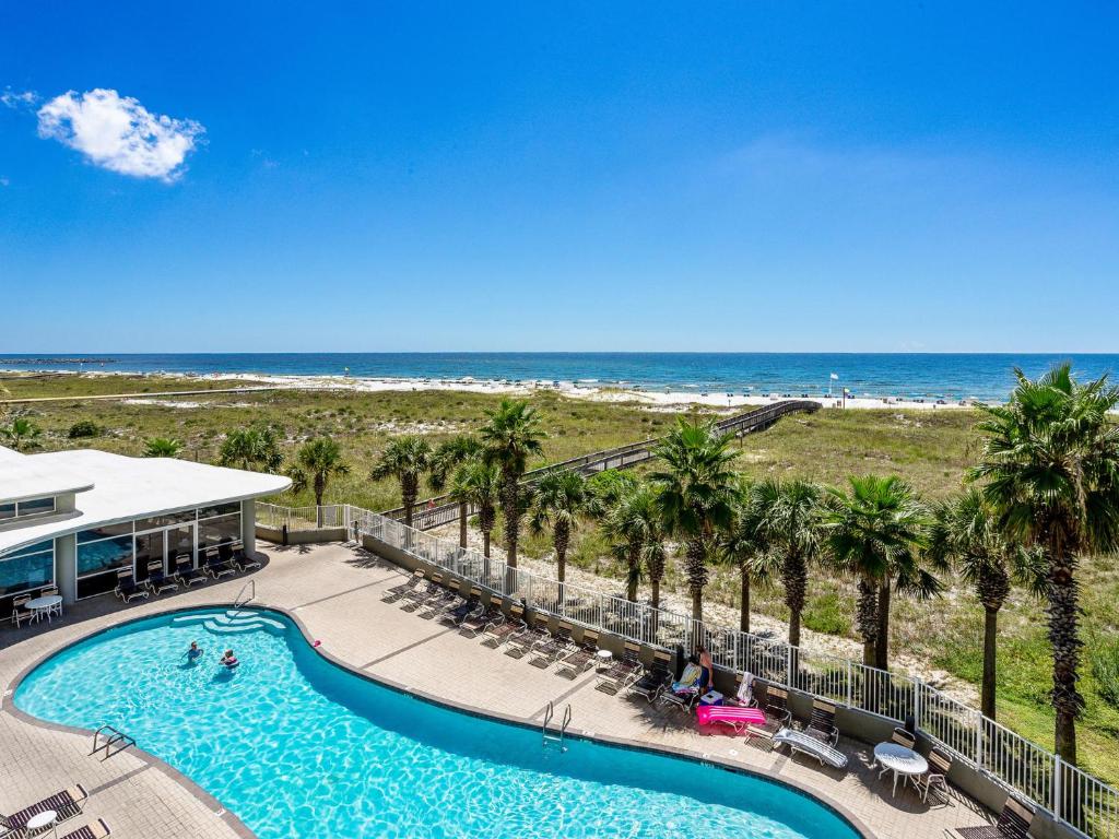 a swimming pool with palm trees and the beach at Tidewater orange Beach 209 in Orange Beach