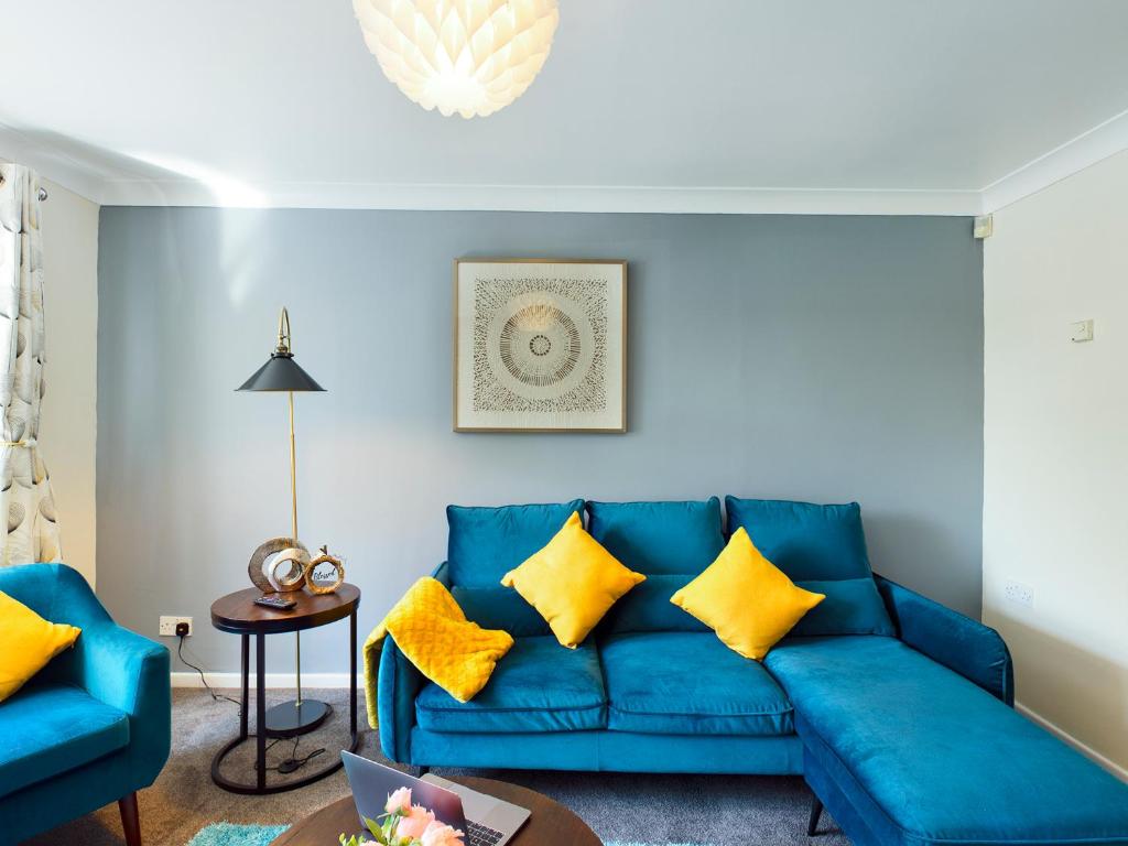 Sofá azul en la sala de estar con almohadas amarillas en 247 Serviced Accommodation in Telford- 3BR HOUSE en Telford