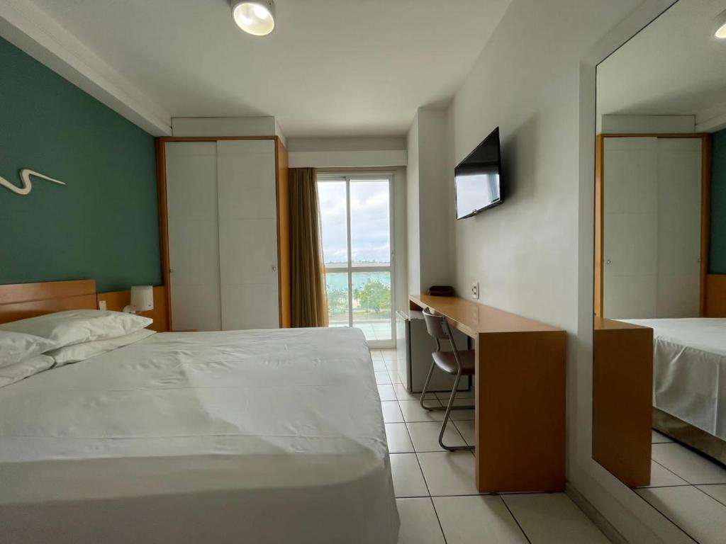 Schlafzimmer mit einem Bett, einem Schreibtisch und einem Fenster in der Unterkunft Thuis I Studio Espetacular na Praia do Canto in Vitória