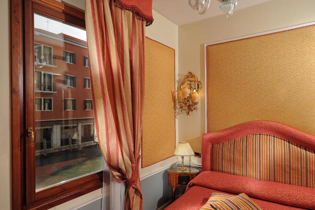 a bedroom with a red chair and a window at Hotel Arlecchino in Venice