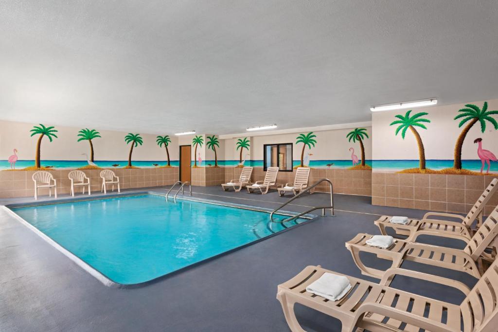 uma piscina do hotel com cadeiras e palmeiras na parede em Days Inn by Wyndham Kansas City International Airport em Kansas City