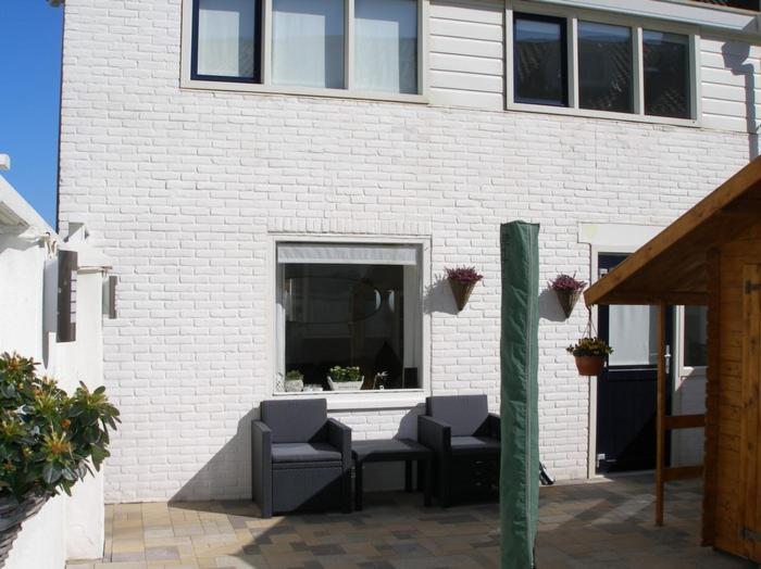 een wit bakstenen gebouw met 2 stoelen en een raam bij Piet's Beachhouse in Katwijk aan Zee