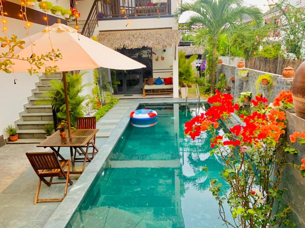 a pool with a table and chairs and red flowers at An Bang Star Homestay in Hoi An