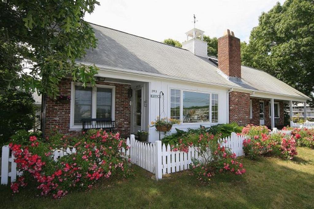 una piccola casa con una recinzione bianca e fiori di Skaket Beach Motel a Orleans