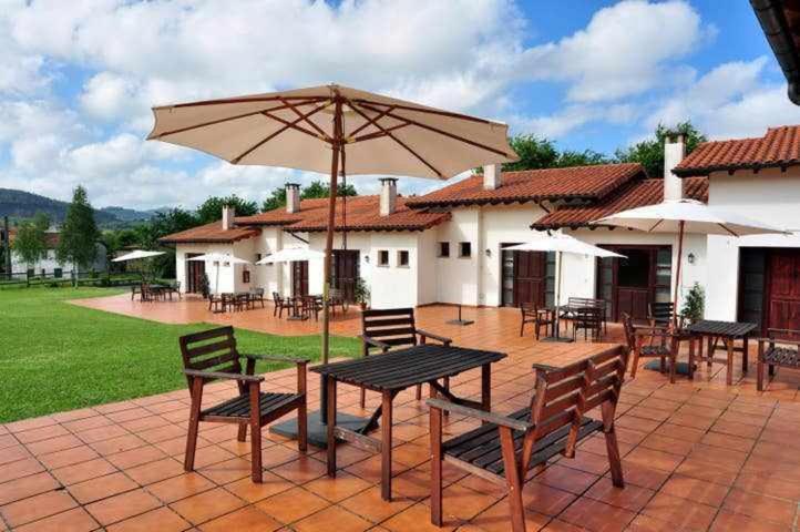 eine Terrasse mit Tischen, Stühlen und einem Sonnenschirm in der Unterkunft Apartamento familiar cercano a playa de Rodiles 1 in Selorio