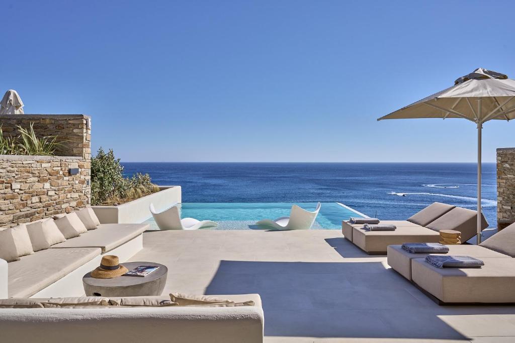 a patio with chairs and an umbrella and the ocean at Ios Grand Pool Suites in Mylopotas
