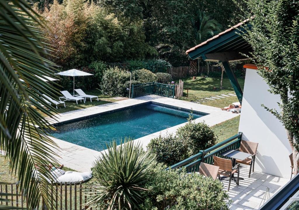 una piscina en un patio con 2 sillas y una sombrilla en Hôtel Les Frères Ibarboure, en Bidart