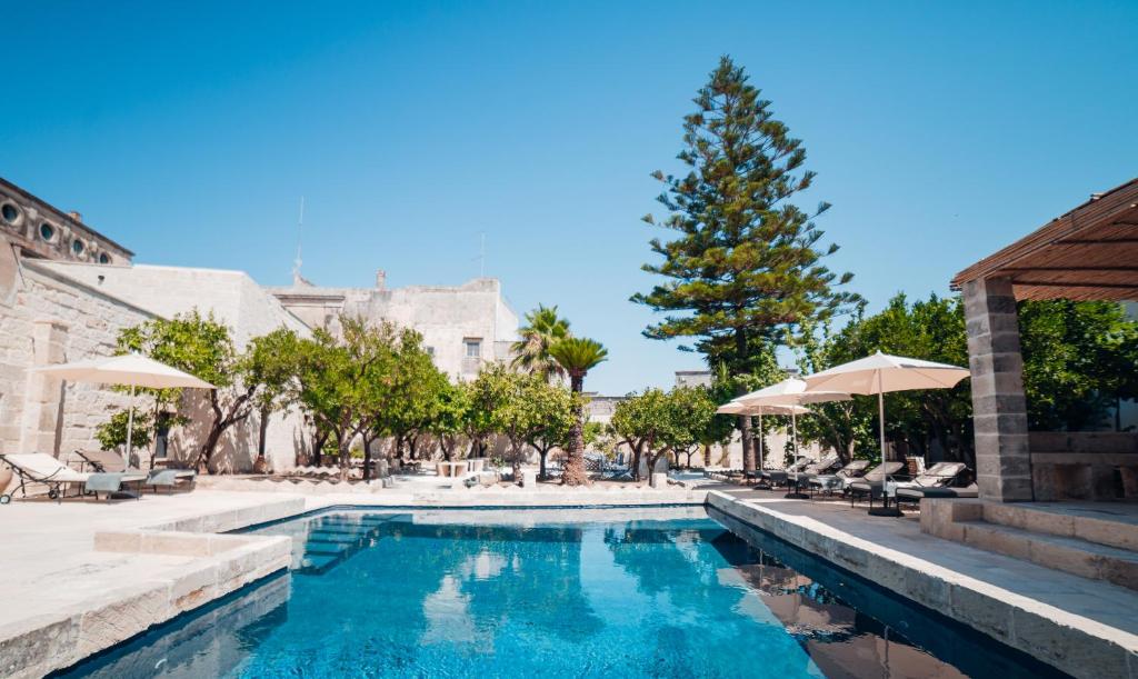 uma piscina com guarda-sóis e cadeiras e uma árvore em Tenuta Tresca Suites - Dimora Storica em San Cassiano