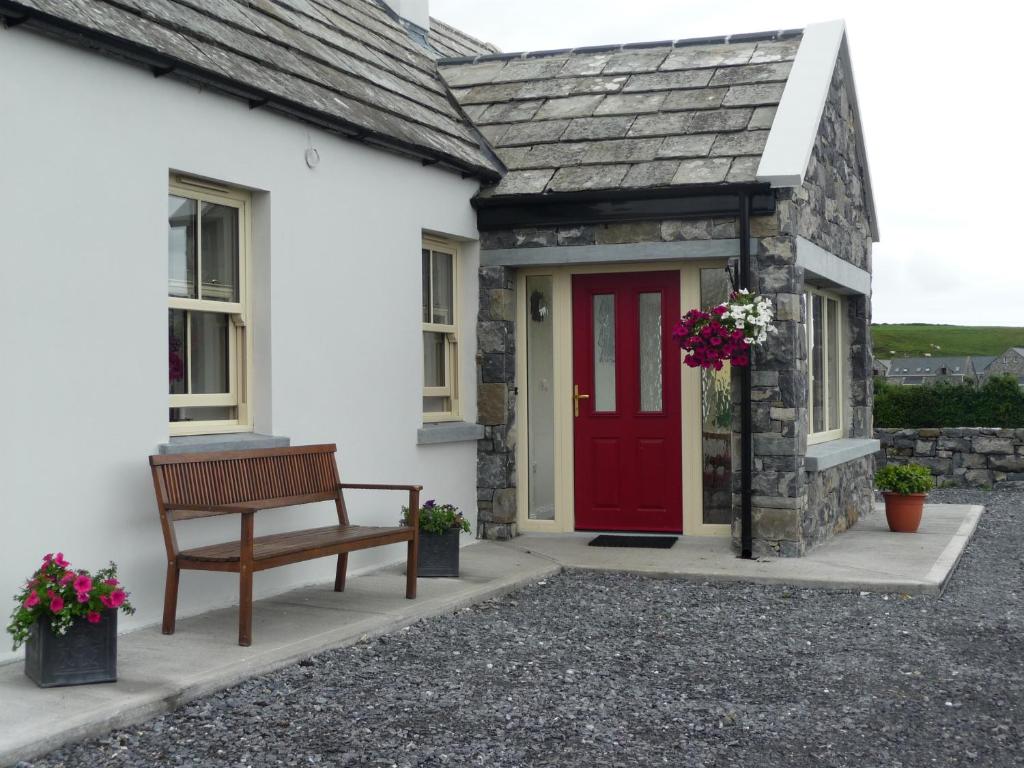 a bench in front of a white house with a red door at Cois Na hAbhann in Doolin