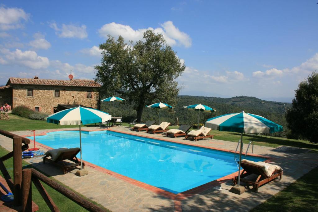 a swimming pool with chairs and umbrellas in front of a house at Podere della Crocchia in Ciggiano