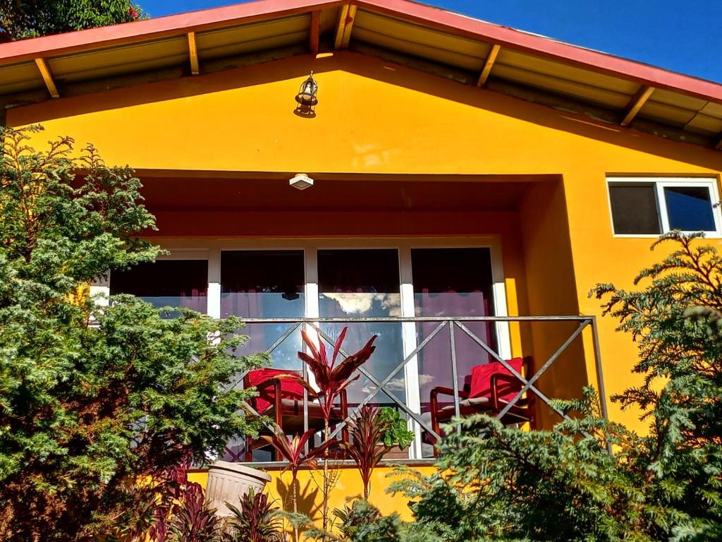 Casa amarilla con sillas rojas en el balcón en Cabañas El Parador en Boquete