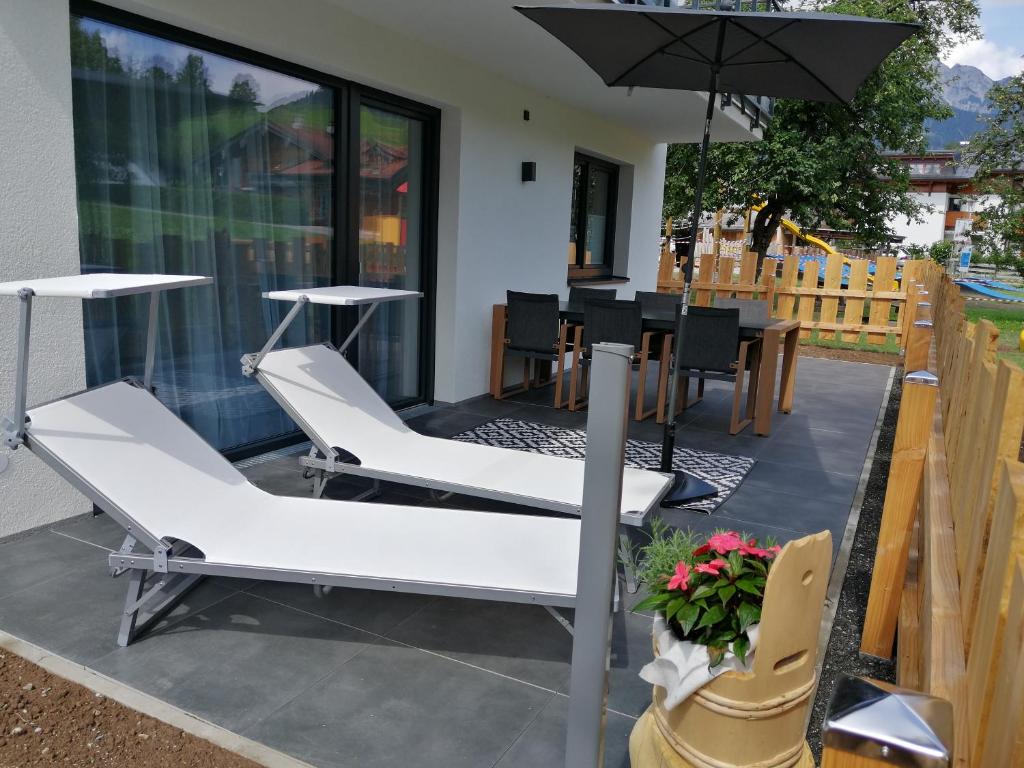 un patio con sillas blancas y una sombrilla en Das Prinzenberg Appartement en Maria Alm am Steinernen Meer