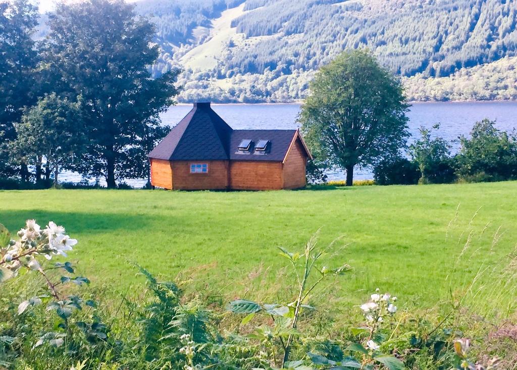 a small house in a field next to a lake at Seal Point Cabin - Luxury Glamping in Cairndow