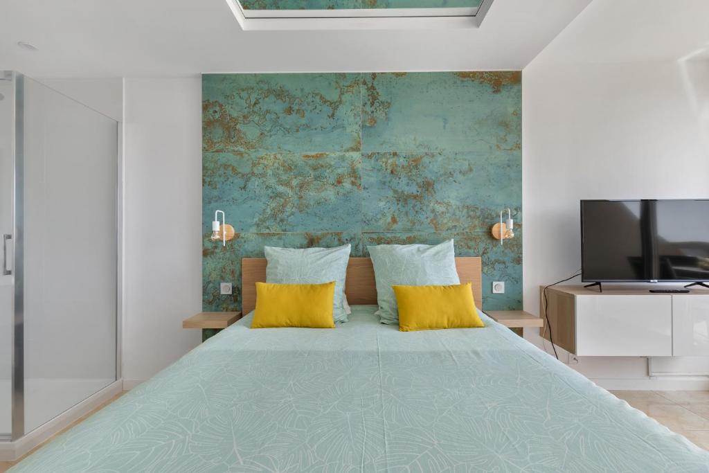 - une chambre avec un lit doté d'oreillers jaunes et une télévision dans l'établissement Azur Heliopolis naturiste, au Cap d'Agde