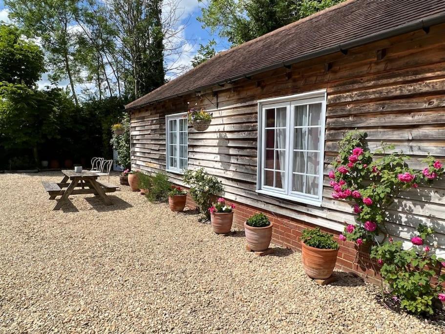 a wooden cabin with potted plants and a picnic table at The Old Estate Office - Enchanting, Stylish Garden Cottage, Peaceful & Quiet in Hurley