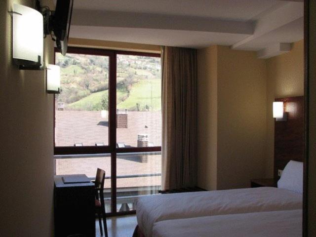 ein Hotelzimmer mit einem Bett und einem großen Fenster in der Unterkunft Hotel Ruta de la Plata de Asturias in Pola de Lena