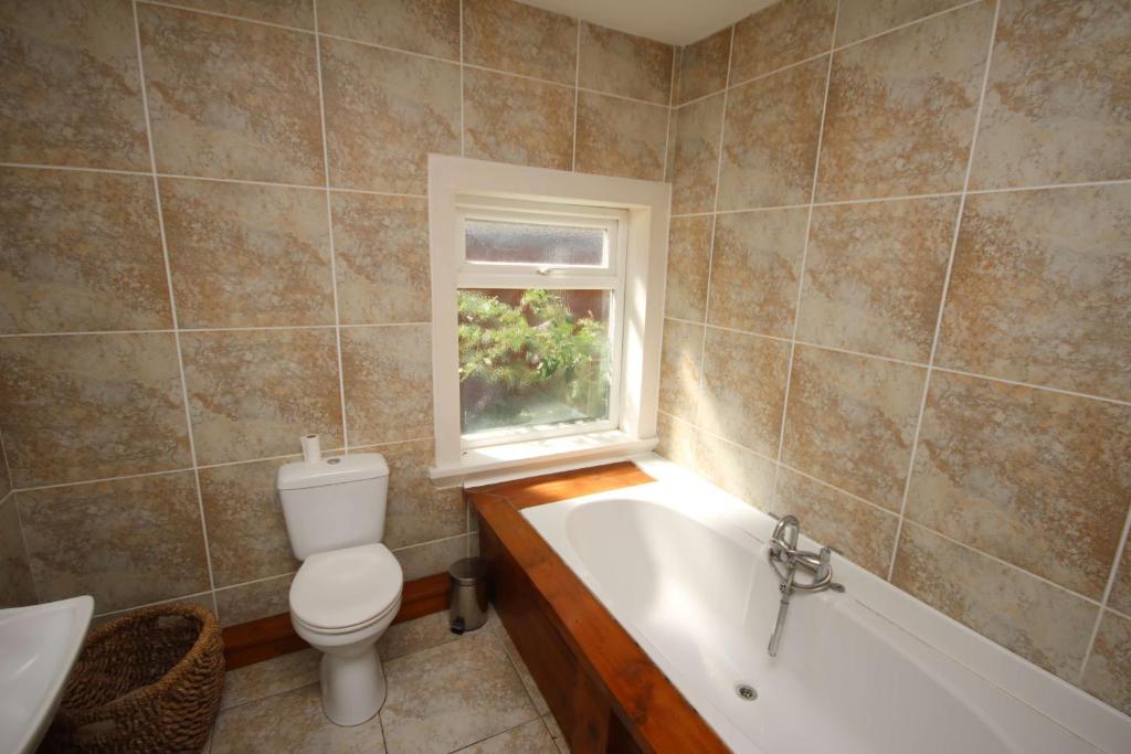 La salle de bains est pourvue de toilettes, d'une baignoire et d'une fenêtre. dans l'établissement Peaceful Bournemouth Family Retreat, à Bournemouth