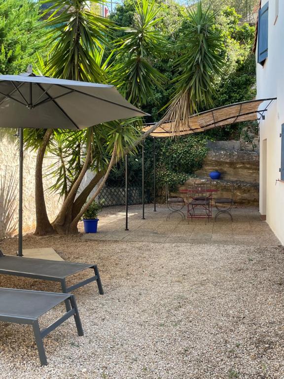 un patio con bancos, sombrilla y mesas en Appartement indépendant Bas de villa avec parking privatif, en La Ciotat