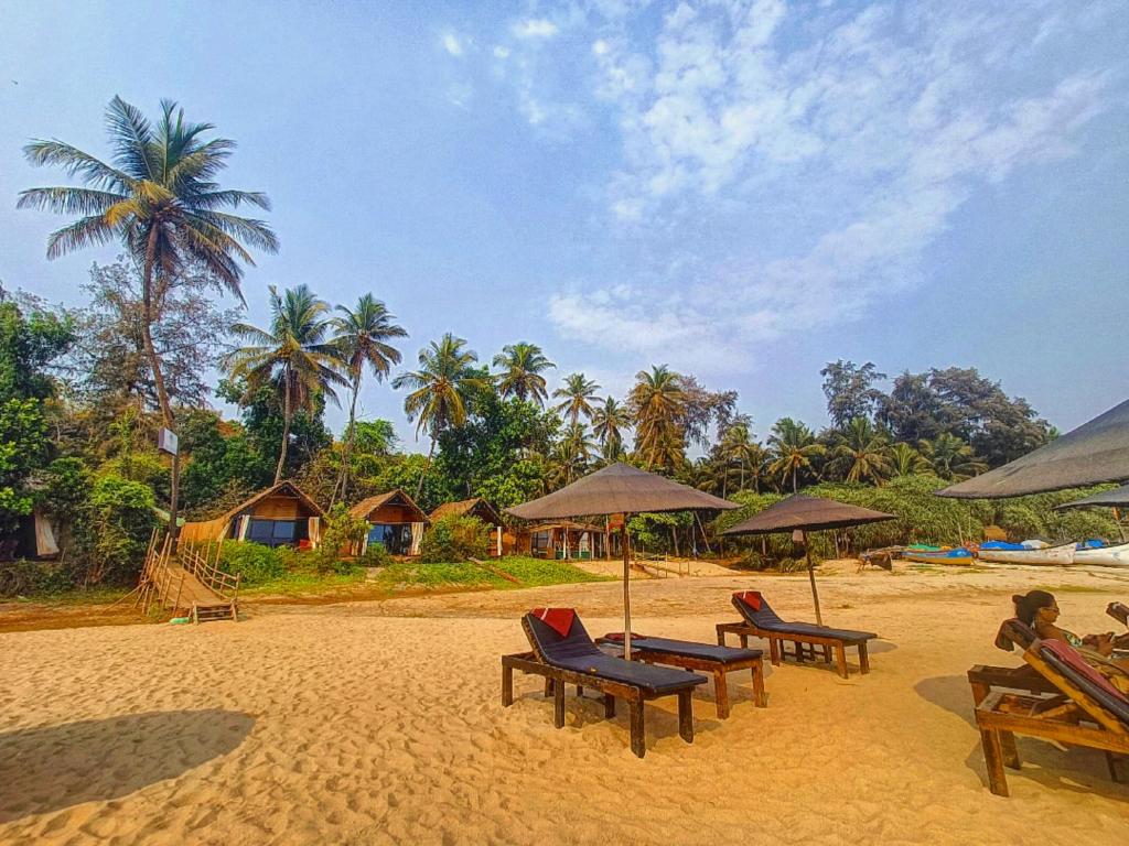 a beach with chairs and umbrellas and palm trees at Nada Brahma Patnem Beach in Patnem