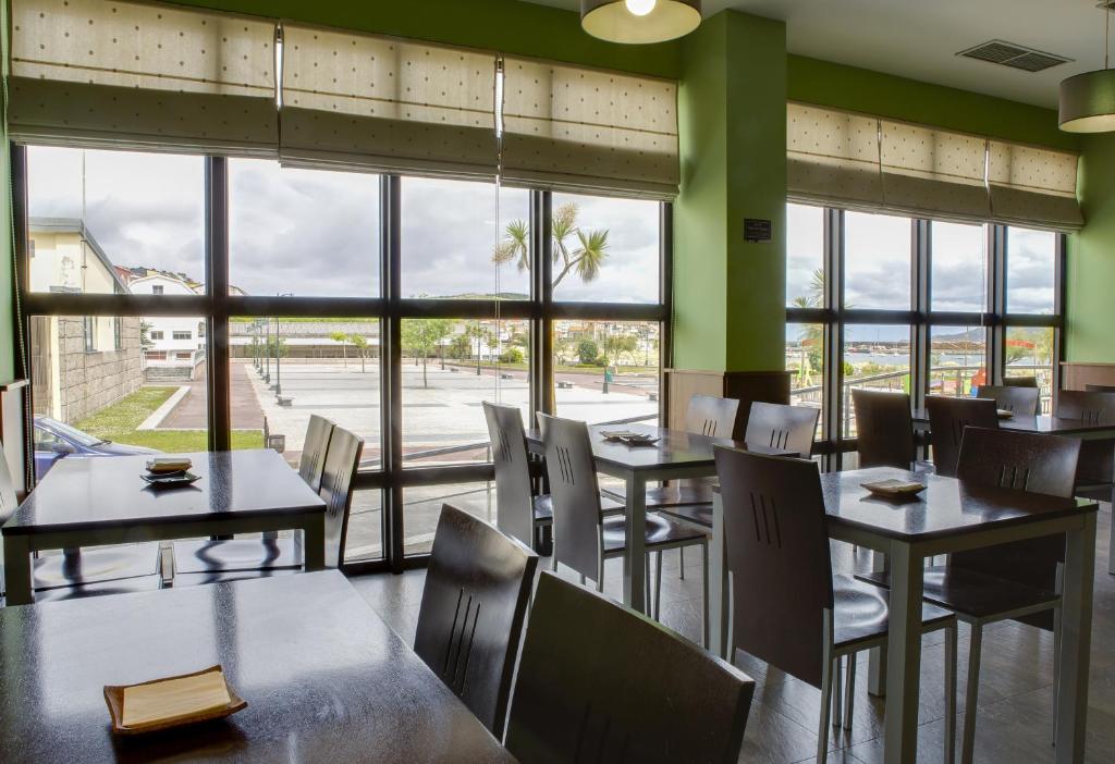 un restaurante con mesas, sillas y ventanas grandes en Hotel Playa de Laxe, en Laxe