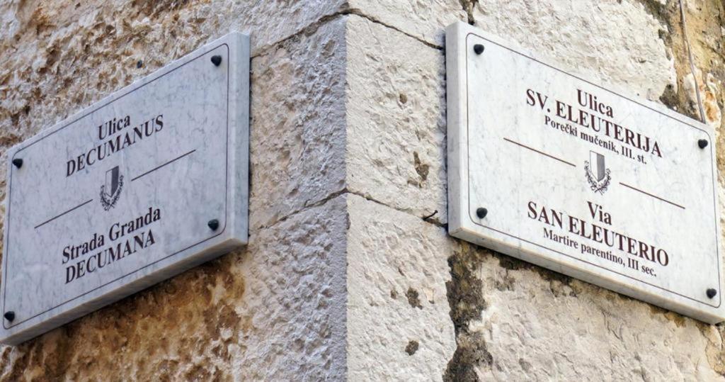two signs on the side of a stone wall at San Eleuterio Guesthouse in Poreč