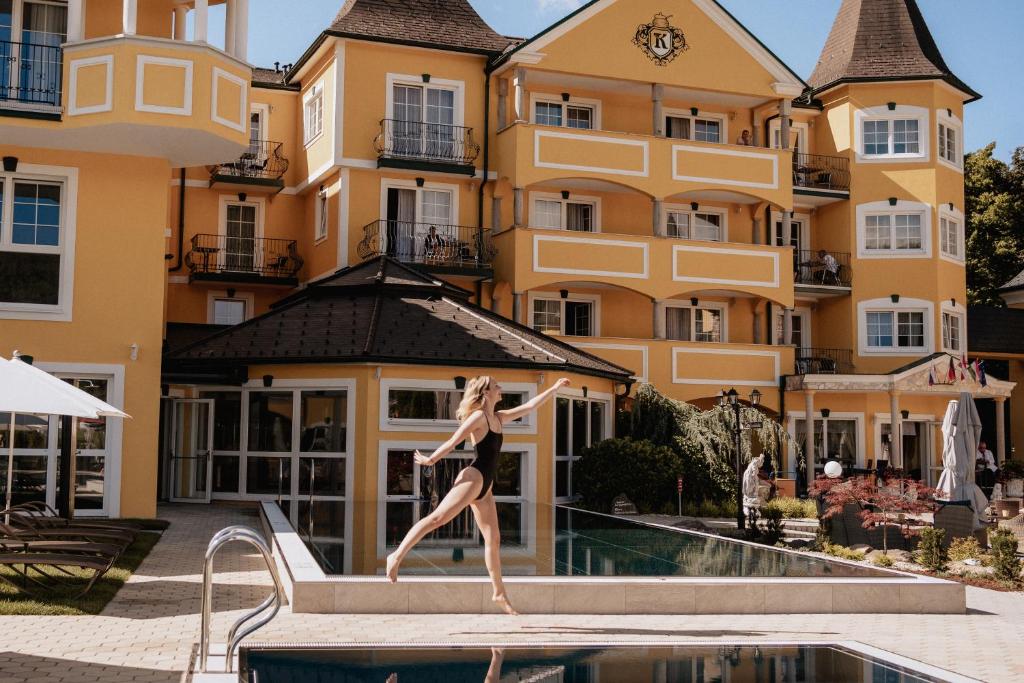 una mujer parada en el borde de una piscina frente a un edificio en Schlössl Hotel Kindl, en Bad Gleichenberg