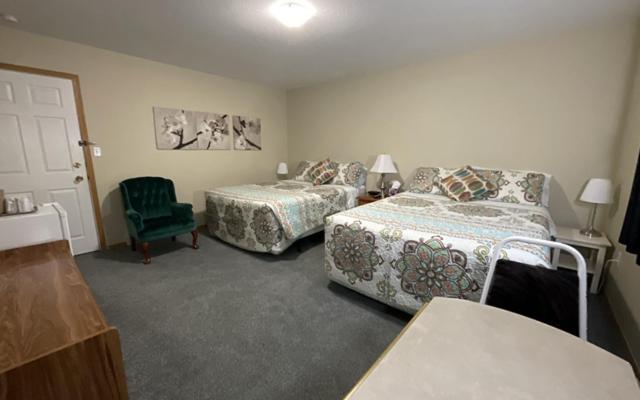 een slaapkamer met 2 bedden en een groene stoel bij NEWCASTLE COUNTRY INN in Drumheller