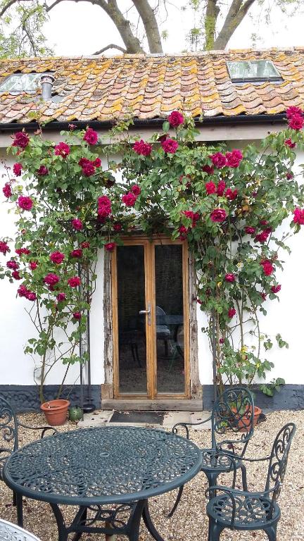 une table et des chaises devant un bâtiment avec des roses dans l'établissement The Granary, à Hardwick