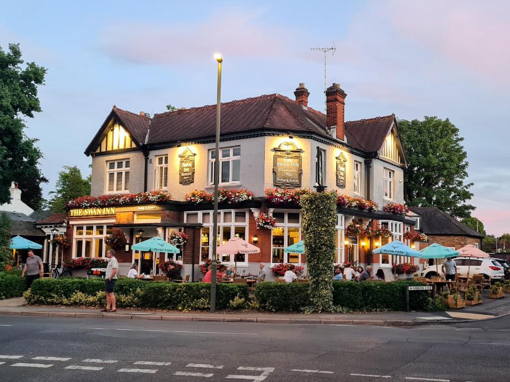 a building with tables and umbrellas on a street at José Pizarro The Swan Inn in Esher